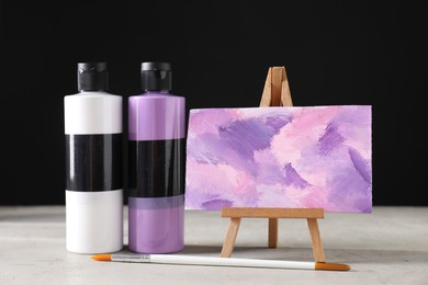 Acrylic paints of different colors in bottles, brush and small easel with abstract picture on light table