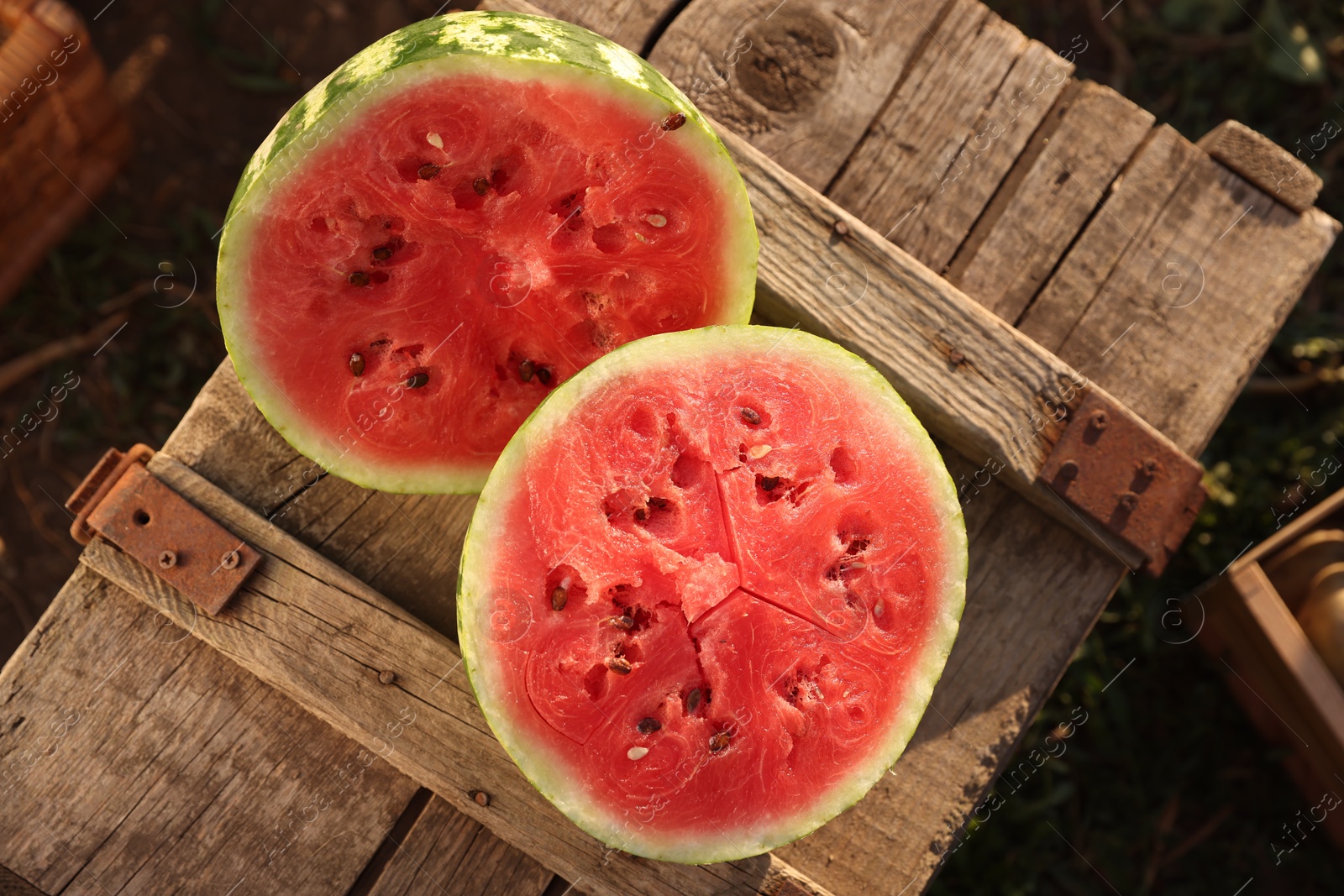 Photo of Halves of ripe watermelon on wooden crate outdoors, top view