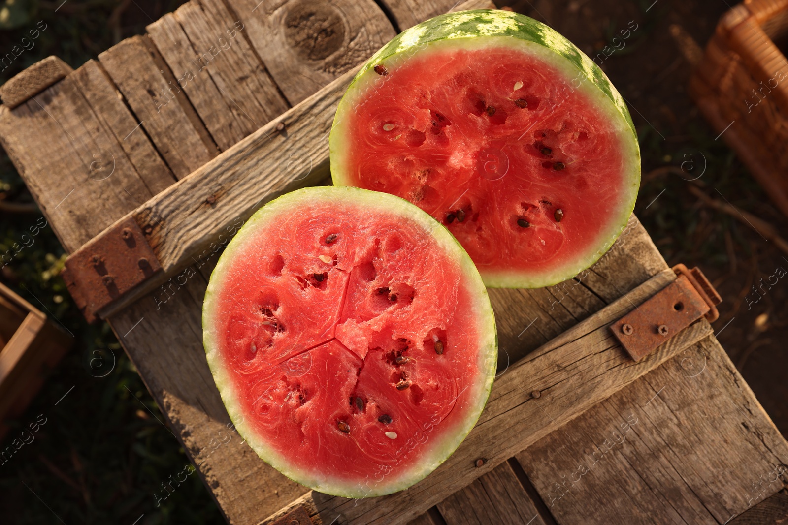 Photo of Halves of ripe watermelon on wooden crate outdoors, top view