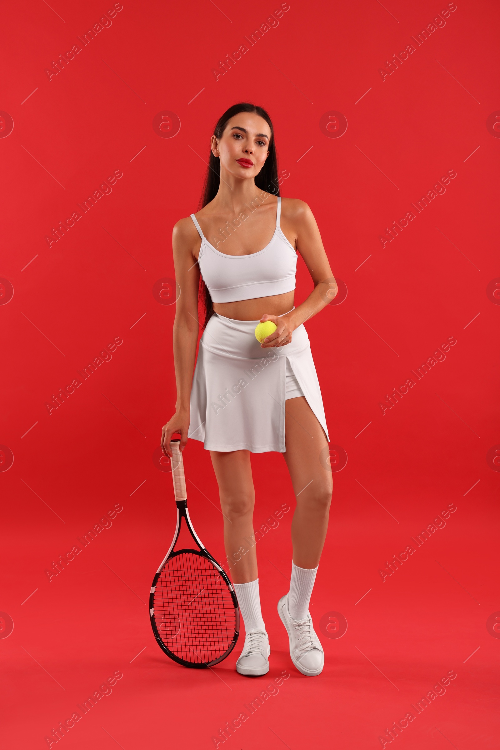 Photo of Beautiful young woman with tennis racket and ball on red background