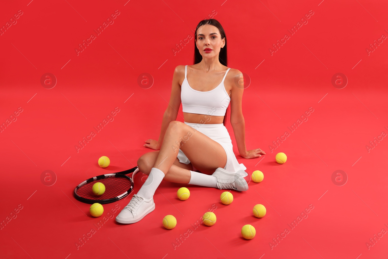 Photo of Beautiful young woman with tennis racket and balls on red background