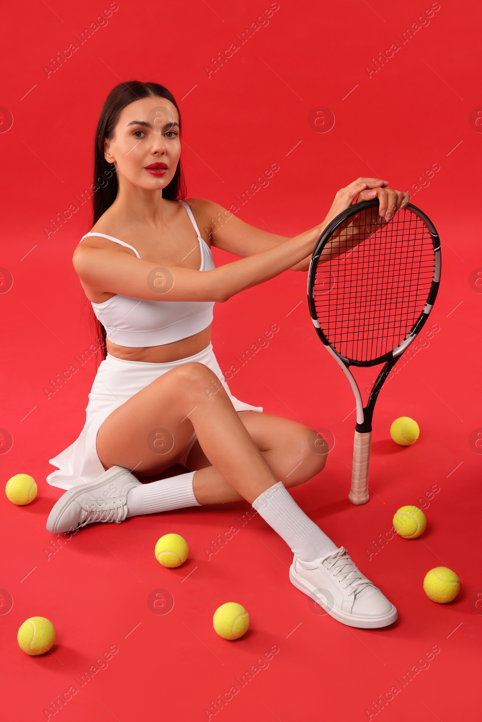 Photo of Beautiful young woman with tennis racket and balls on red background