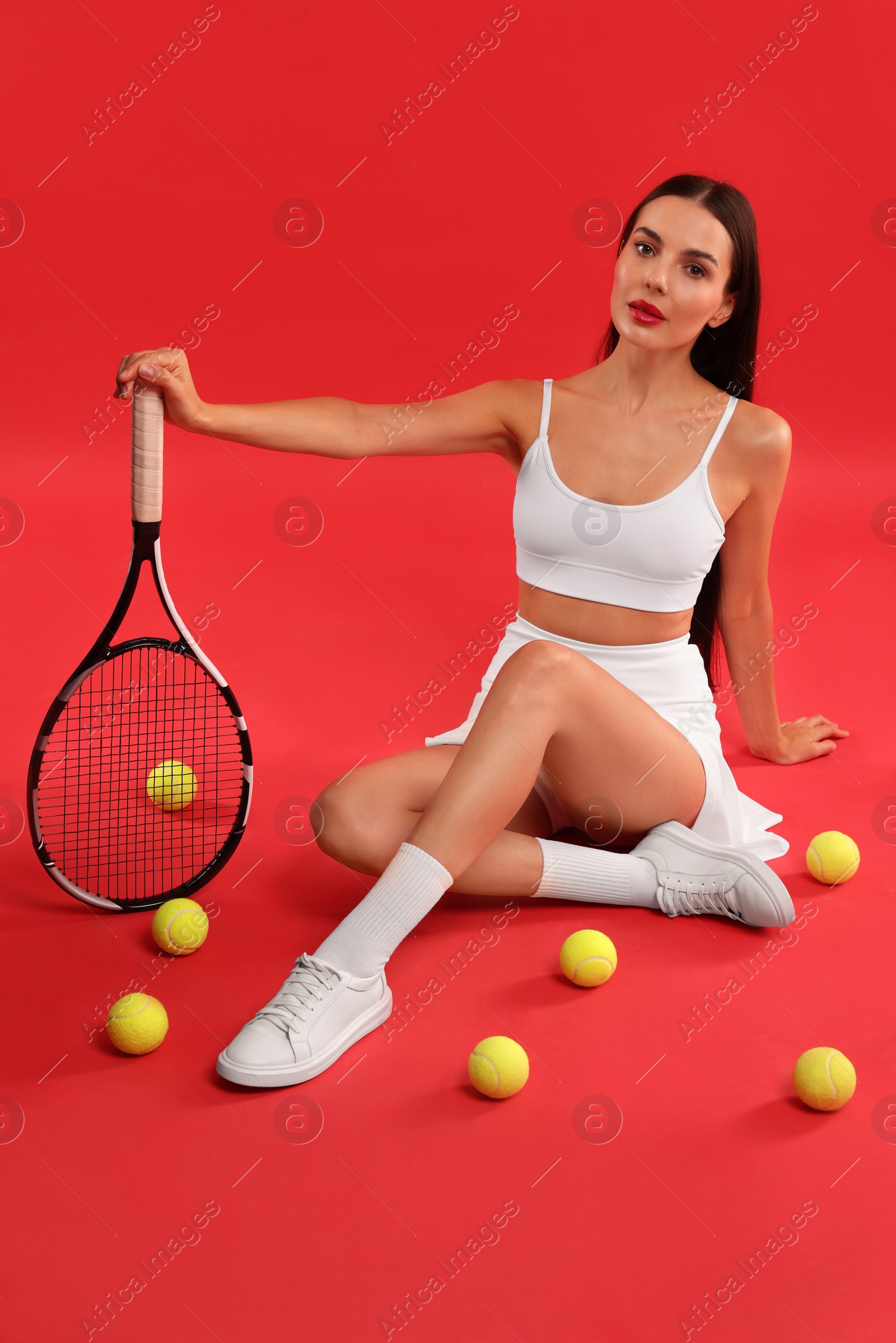 Photo of Beautiful young woman with tennis racket and balls on red background