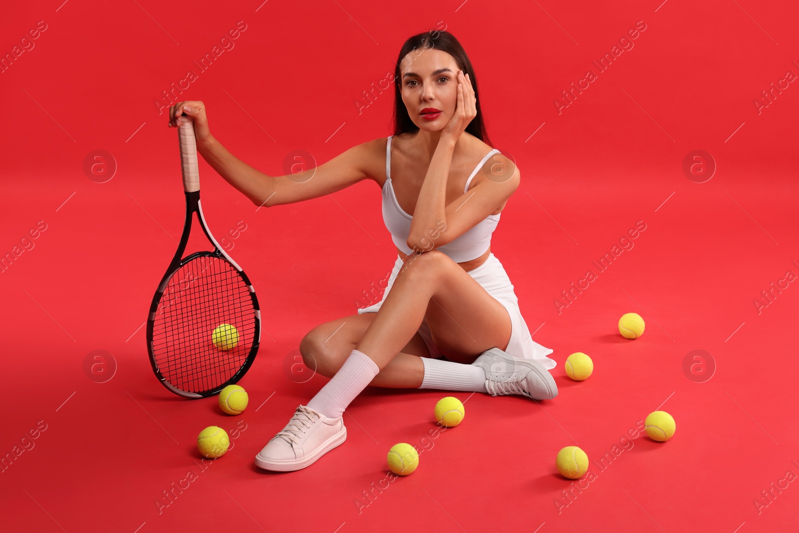 Photo of Beautiful young woman with tennis racket and balls on red background