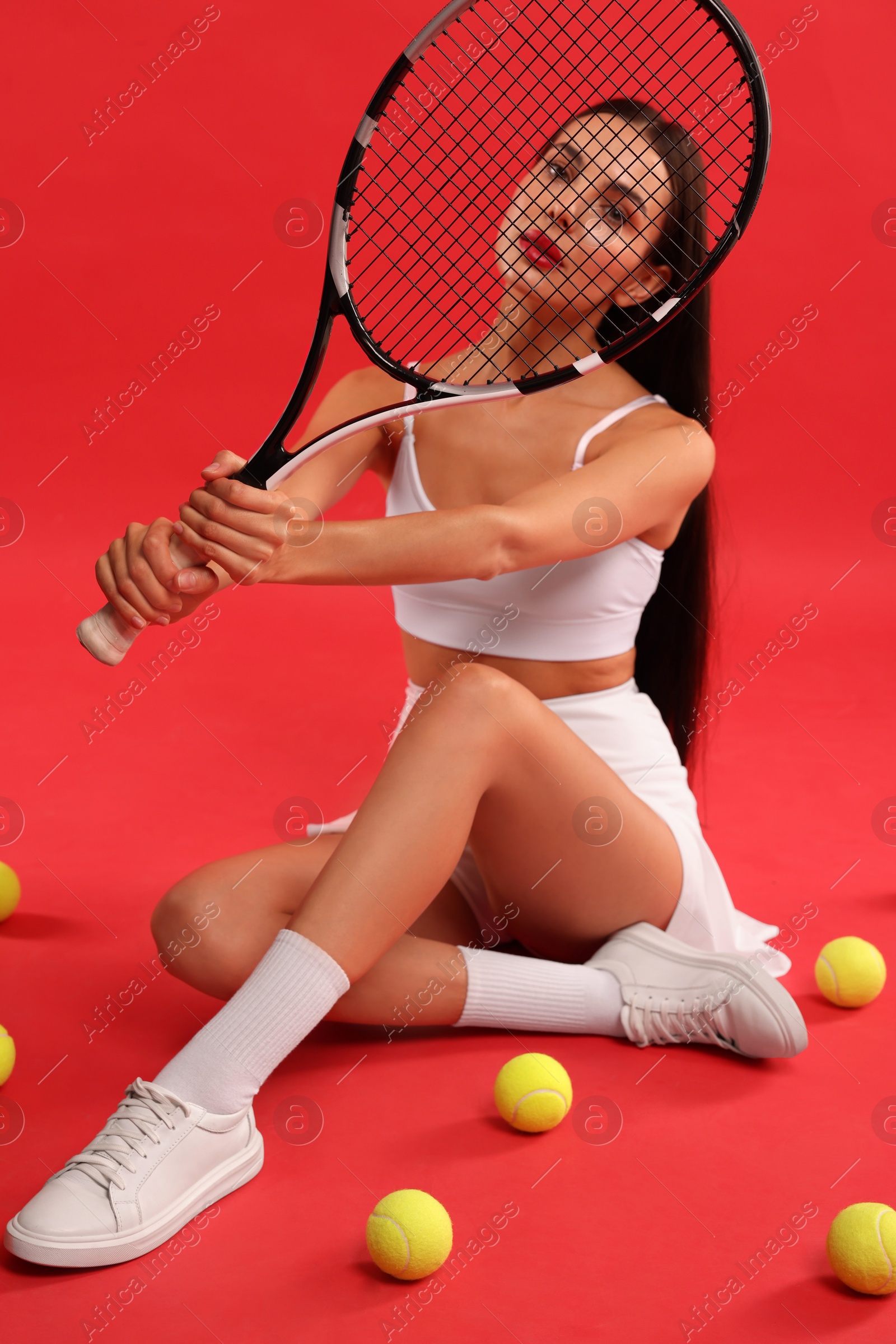 Photo of Beautiful young woman with tennis racket and balls on red background