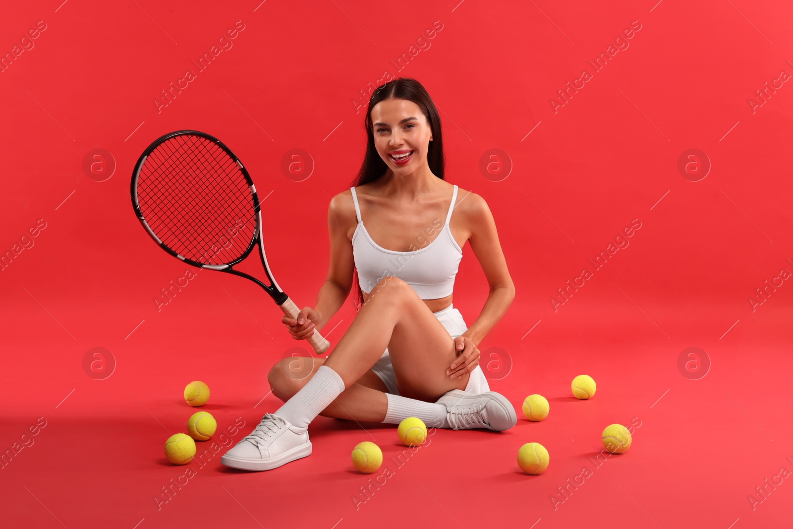 Photo of Beautiful young woman with tennis racket and balls on red background