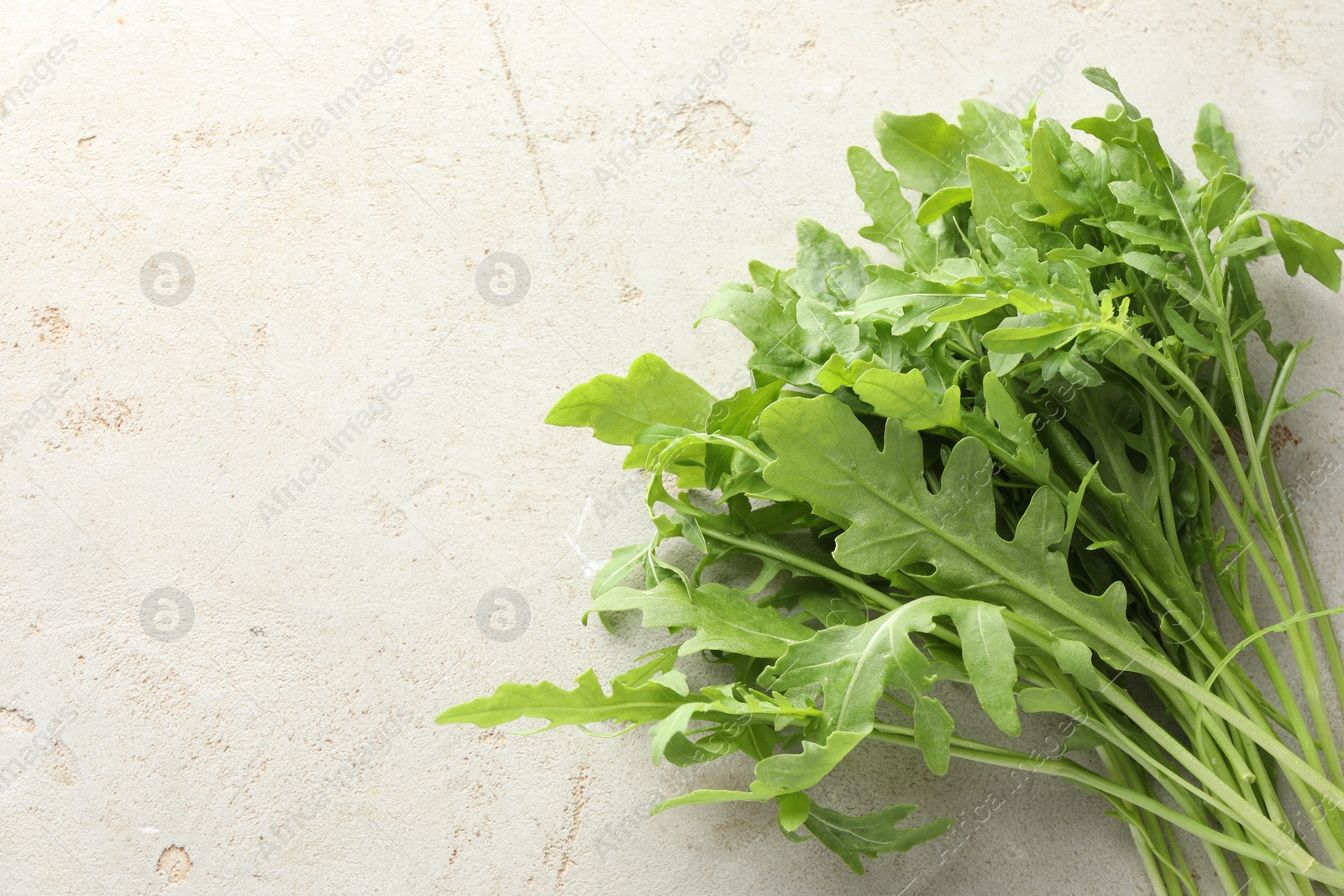 Photo of Many fresh arugula leaves on grey textured table, top view. Space for text