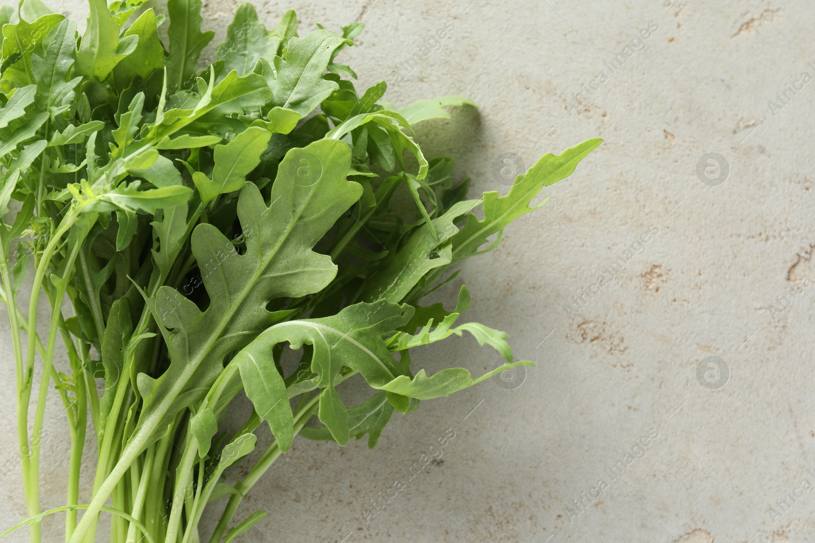 Photo of Many fresh arugula leaves on grey textured table, top view. Space for text