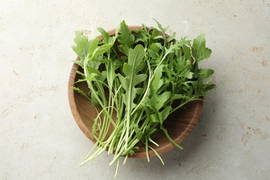 Photo of Many fresh arugula leaves in bowl on grey textured table, top view