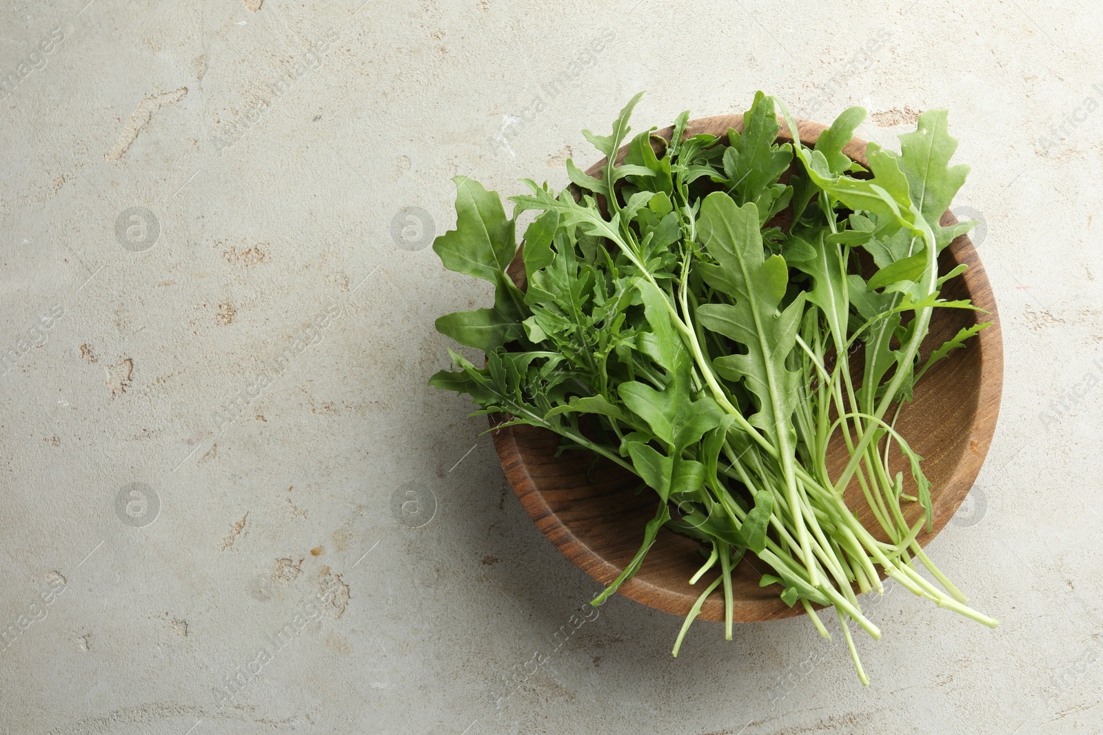 Photo of Many fresh arugula leaves in bowl on grey textured table, top view. Space for text