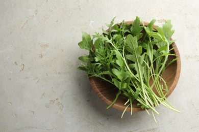 Photo of Many fresh arugula leaves in bowl on grey textured table, top view. Space for text