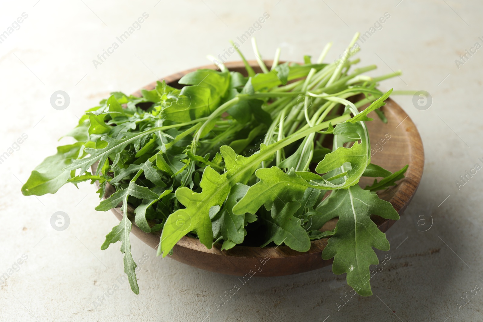 Photo of Many fresh arugula leaves in bowl on grey textured table, closeup