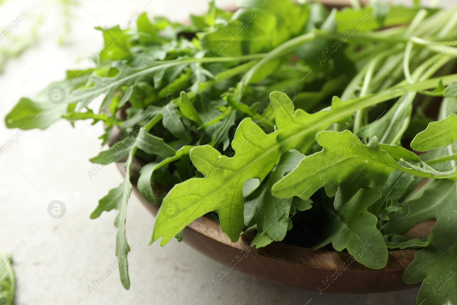 Photo of Many fresh arugula leaves in bowl on grey textured table, closeup