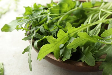 Photo of Many fresh arugula leaves in bowl on grey textured table, closeup