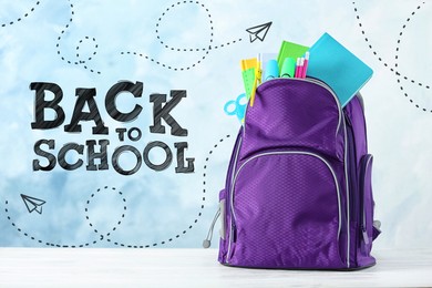 Image of Backpack with stationery on desk against light blue background. Back to school