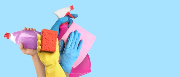 Image of Janitors holding different cleaning supplies on light blue background, closeup. Banner design with space for text