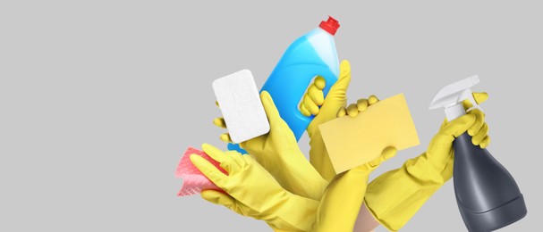 Image of Janitors holding different cleaning supplies on grey background, closeup. Banner design with space for text