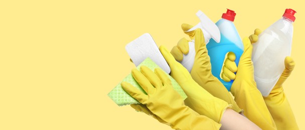 Janitors holding different cleaning supplies on yellow background, closeup. Banner design with space for text