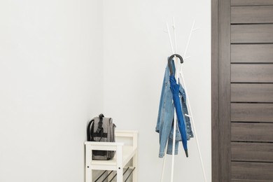 Photo of Blue umbrella and denim jacket on clothing rack near shoe storage bench with backpack in hallway