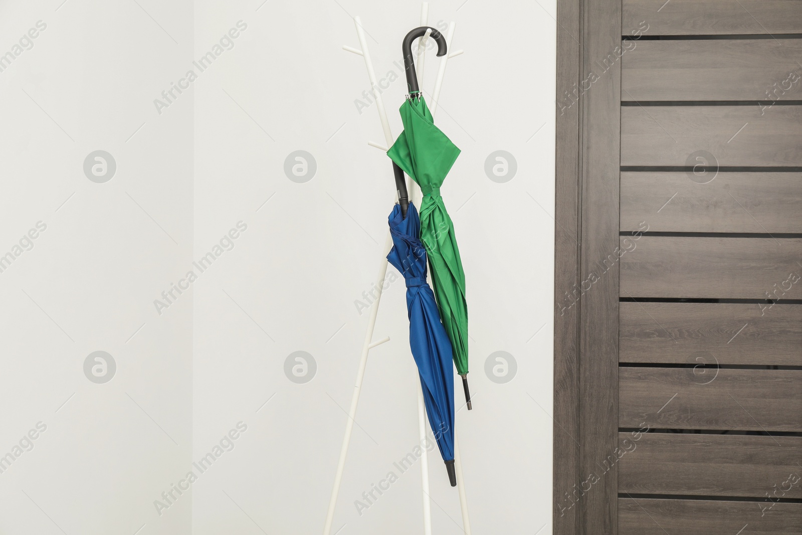 Photo of Colorful umbrellas on clothing rack in hallway, space for text