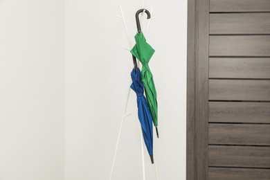 Photo of Colorful umbrellas on clothing rack in hallway, space for text