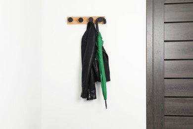 Photo of Green umbrella and leather jacket on rack in hallway