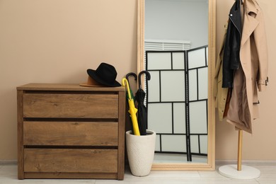 Photo of Colorful umbrellas in holder, rack with coat and jacket indoors