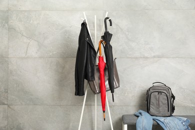 Photo of Colorful umbrellas, jacket and bag on clothing rack near gray marble wall