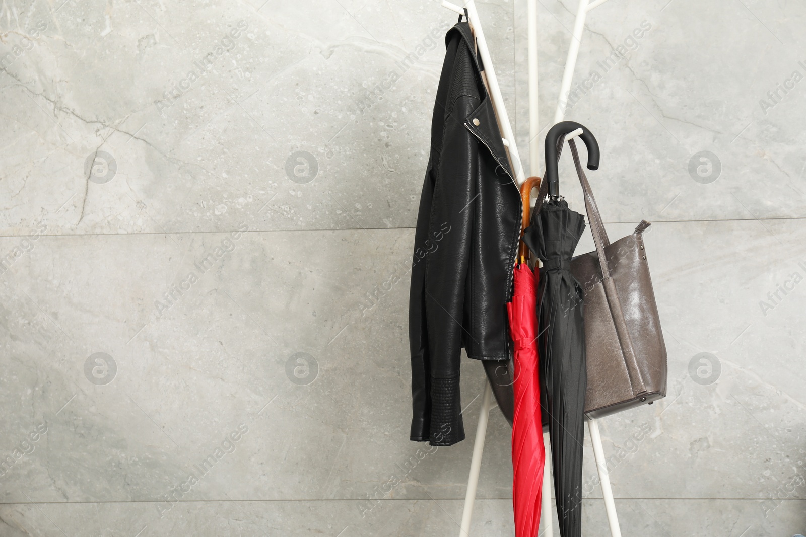 Photo of Colorful umbrellas on rack near gray marble wall, space for text