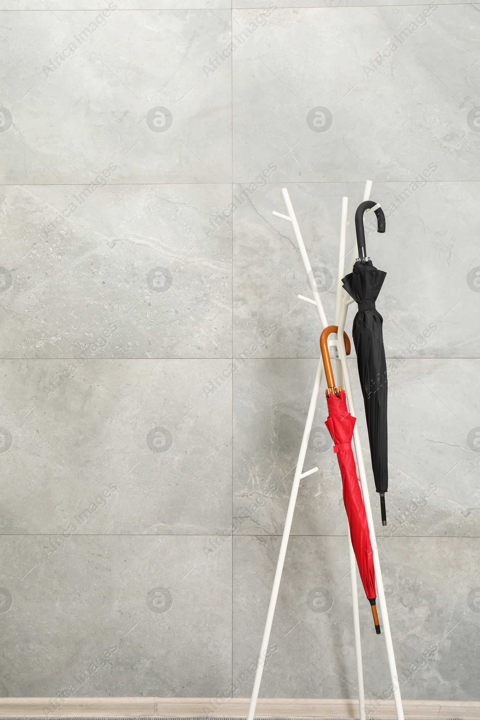 Photo of Colorful umbrellas on rack near gray marble wall