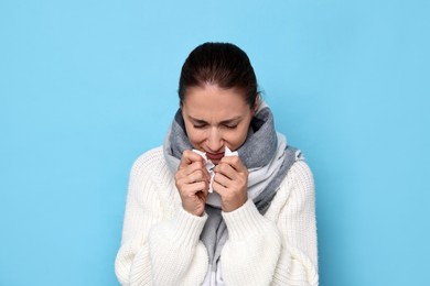 Sick woman with tissue on light blue background. Cold symptoms