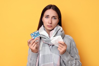 Sick woman with tissue and pills on orange background. Cold symptoms