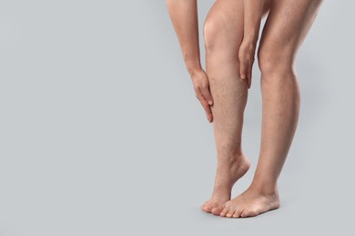 Woman suffering from varicose veins on grey background, closeup. Space for text