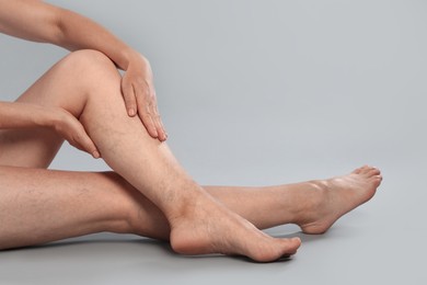 Woman suffering from varicose veins on grey background, closeup