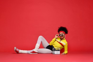 Aerobics. Woman in sportswear holding radio receiver on red background