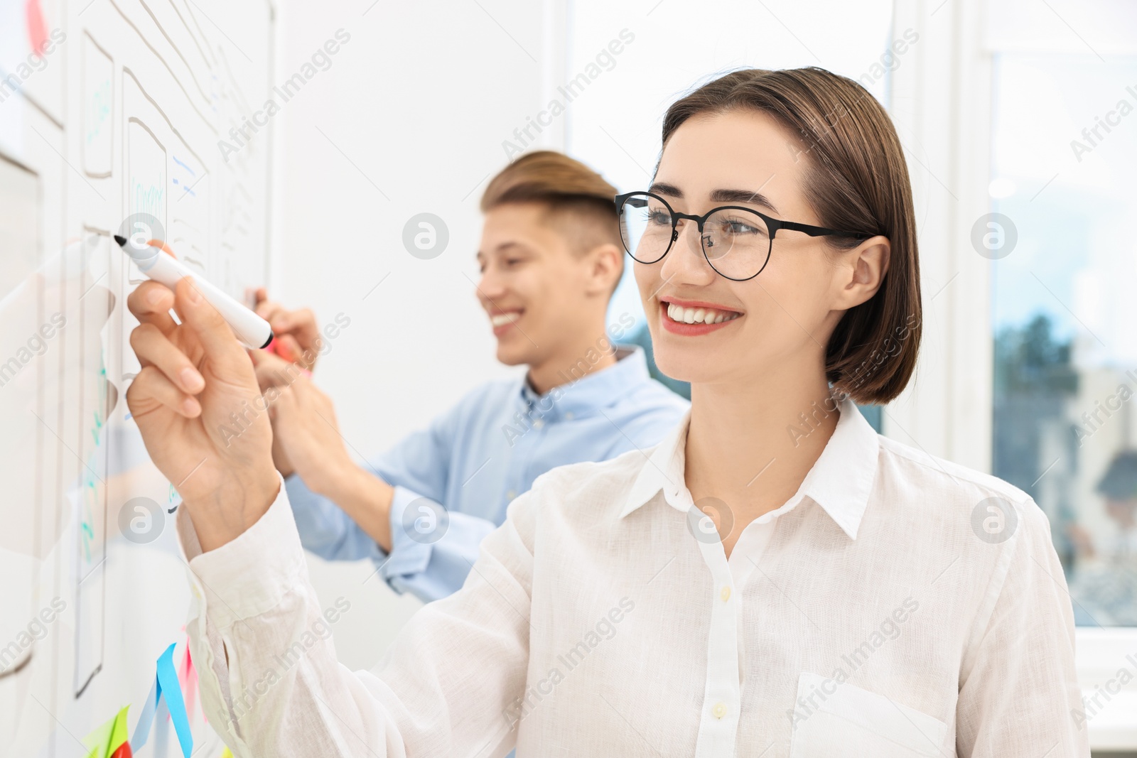 Photo of Developing UI design. Man and woman drawing website wireframe on whiteboard indoors