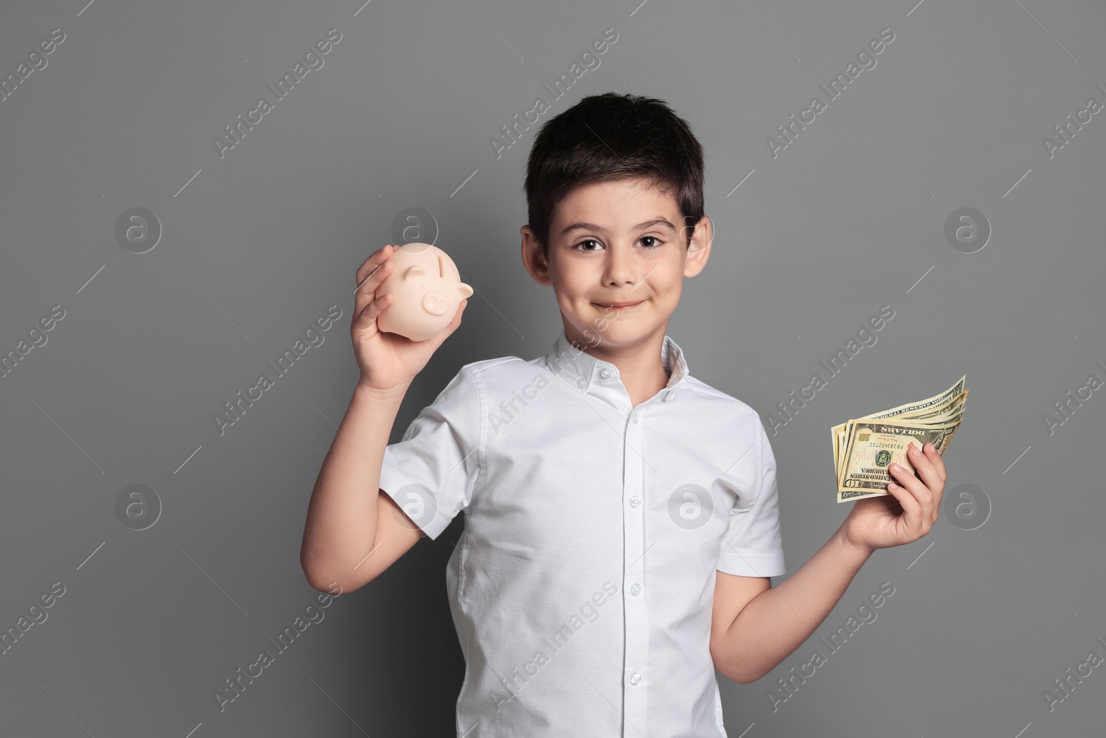 Photo of Cute boy with piggy bank and pocket money on grey background