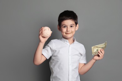 Cute boy with piggy bank and pocket money on grey background