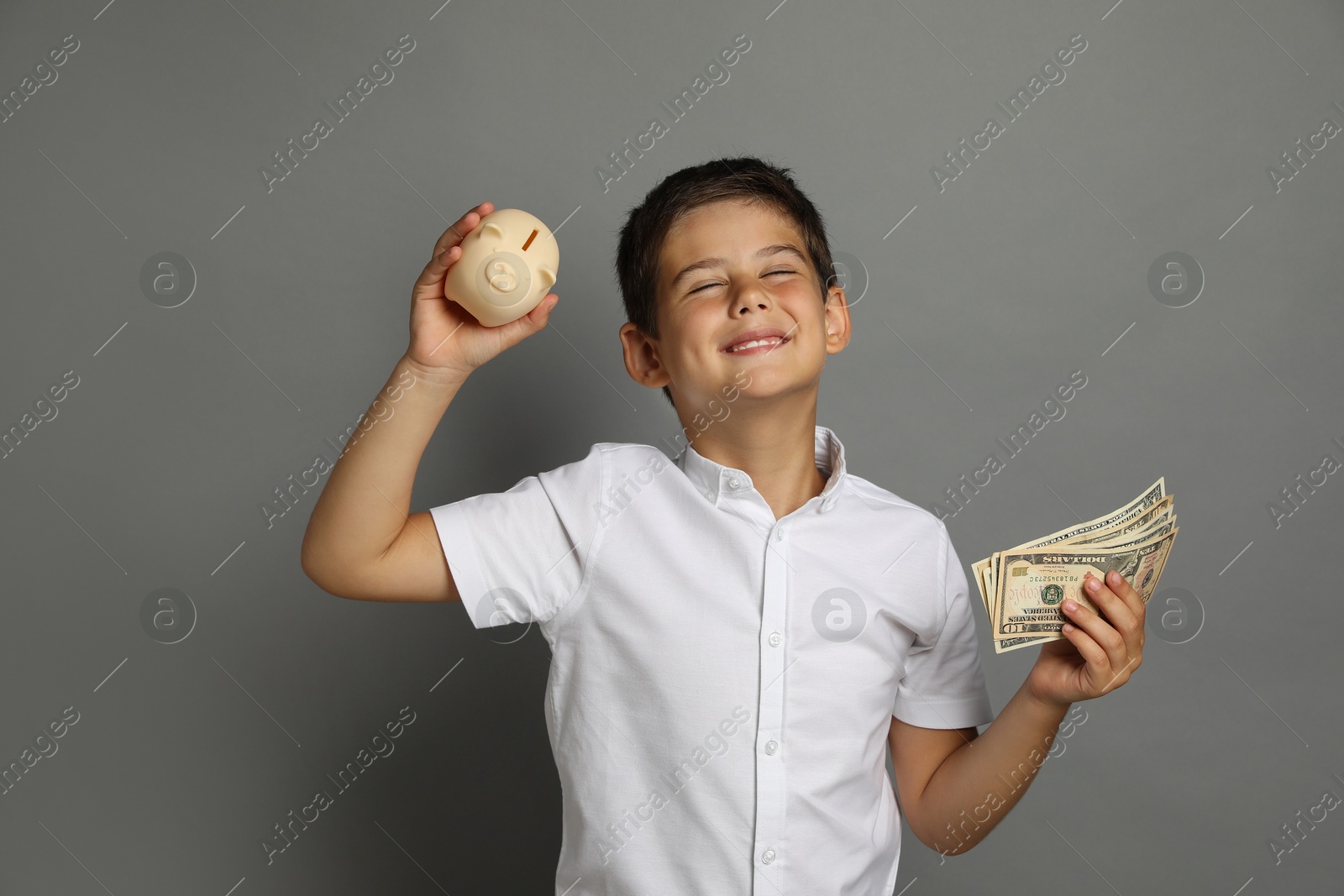 Photo of Cute boy with piggy bank and pocket money on grey background