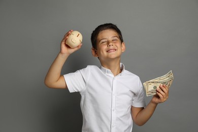 Cute boy with piggy bank and pocket money on grey background