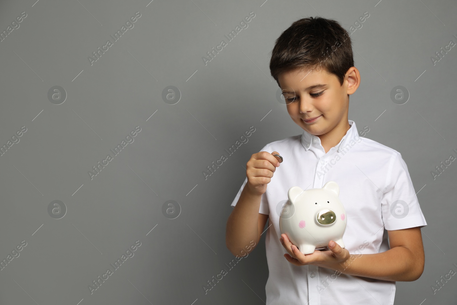 Photo of Pocket money. Cute boy with piggy bank and coins on grey background, space for text