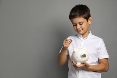 Pocket money. Cute boy with piggy bank and coins on grey background, space for text