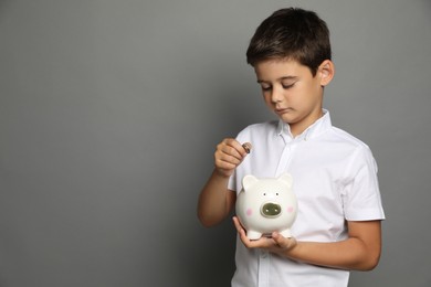 Pocket money. Cute boy with piggy bank and coins on grey background, space for text