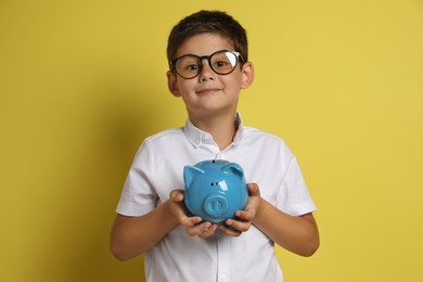 Pocket money. Cute boy with piggy bank on yellow background