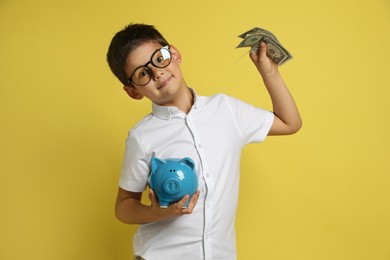 Cute boy with piggy bank and pocket money on yellow background