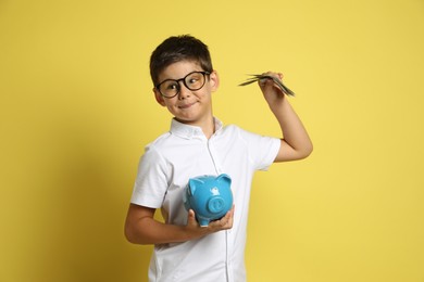 Photo of Cute boy with piggy bank and pocket money on yellow background