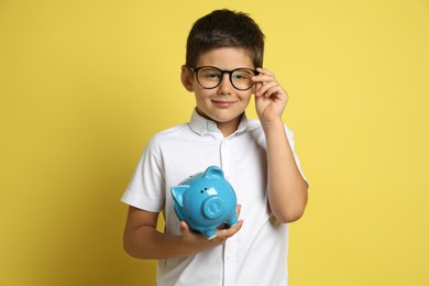 Photo of Pocket money. Cute boy with piggy bank on yellow background