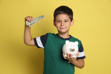 Cute boy with piggy bank and pocket money on yellow background