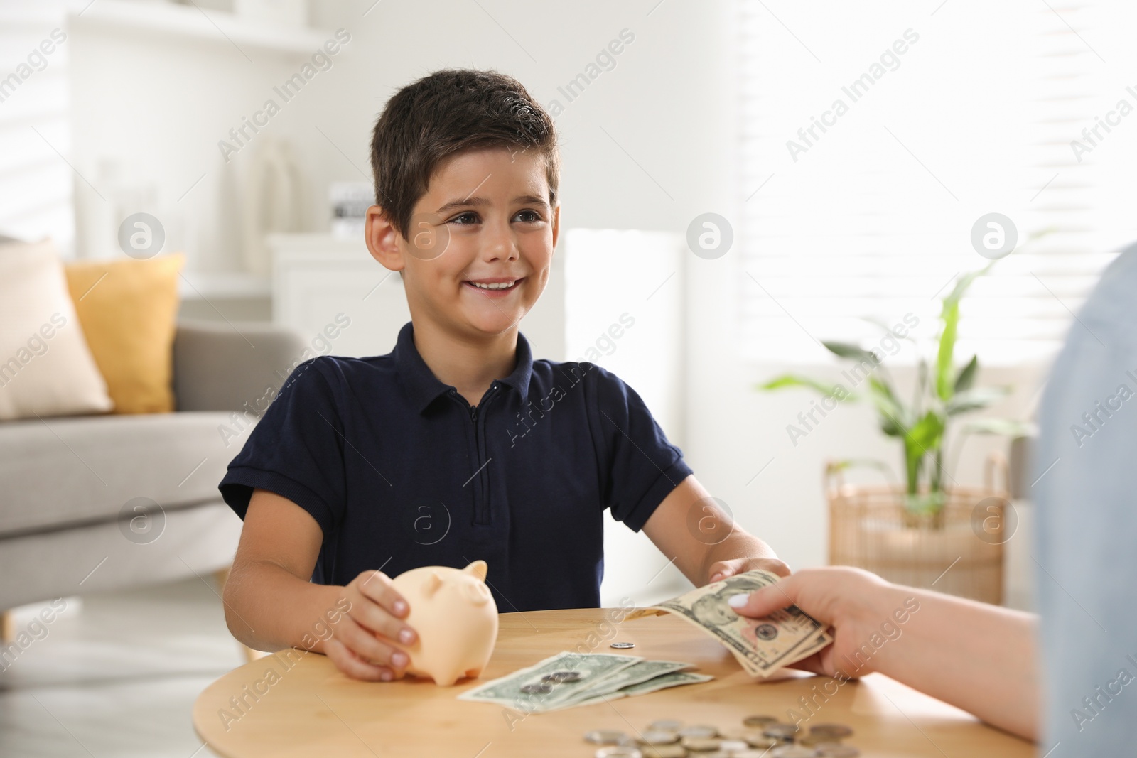 Photo of Mother giving pocket money to her son at table indoors