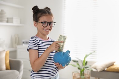 Photo of Cute girl with pocket money and piggy bank at home, space for text